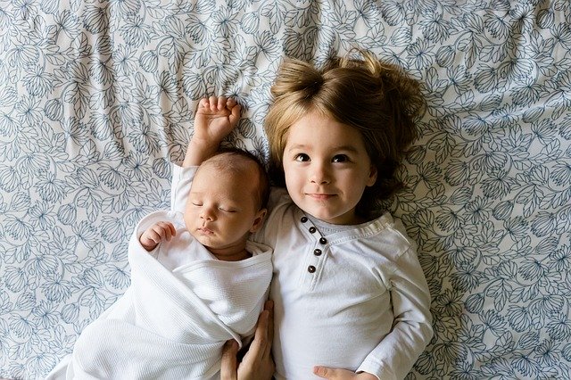 A toddler girl hugging her younger sibling.