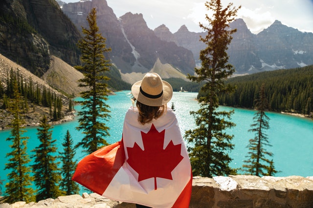 woman wearing a Canadian flag and looking at a beautiful blue lake