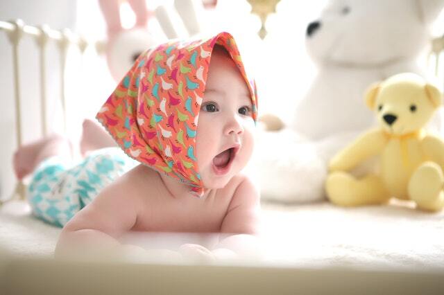 a baby with a scarf opening her mouth in a crib