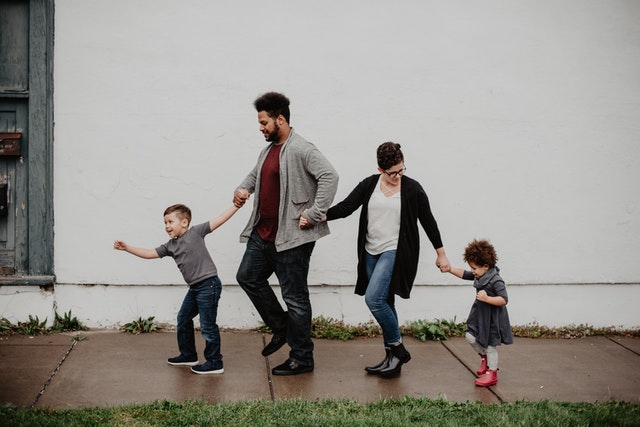a family of four holding hands on the sidewalk