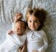 : a small girl and a baby lying on a bed symbolizing things to consider when buying a house with kids