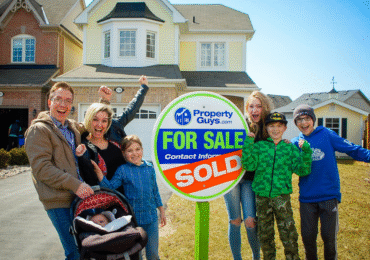 Family happily celebrating the sale of their home in front of a PropertyGuys.com “Sold” sign.